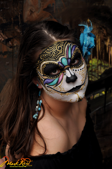 dark haired girl with a gold and blue mask painted around her eyes